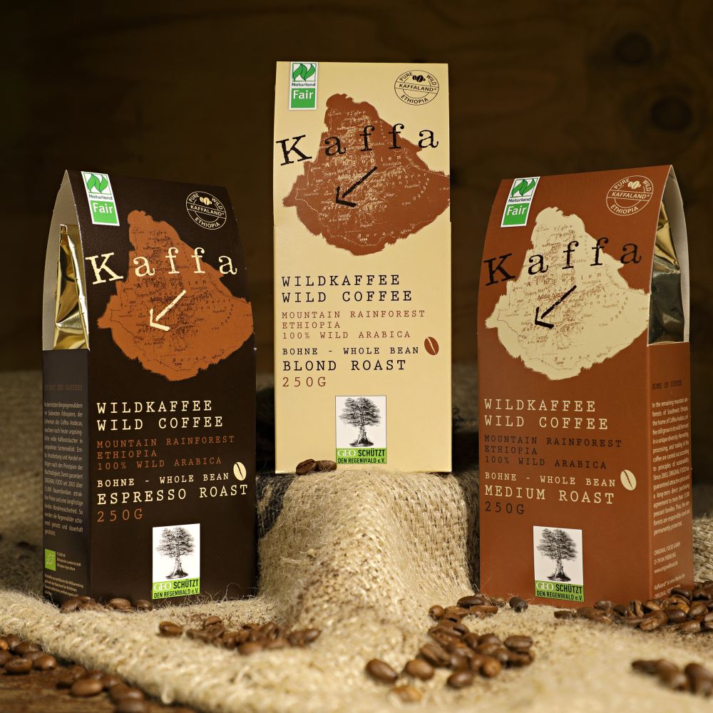 drei  verschiedenfarbige Kafeetüten mit Wildkaffe unterschiedlicher Varianten. Vor den Tüten liegen Kafeebohnen