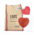 braune Papiertüte, links drei rote Streifen, mittig in Schwarz die Aufschrift "LOVE", oben rechts befindet sich ein roter Papieraufhänger in Herzform, darunter ein Stück rote Seife in Herzform