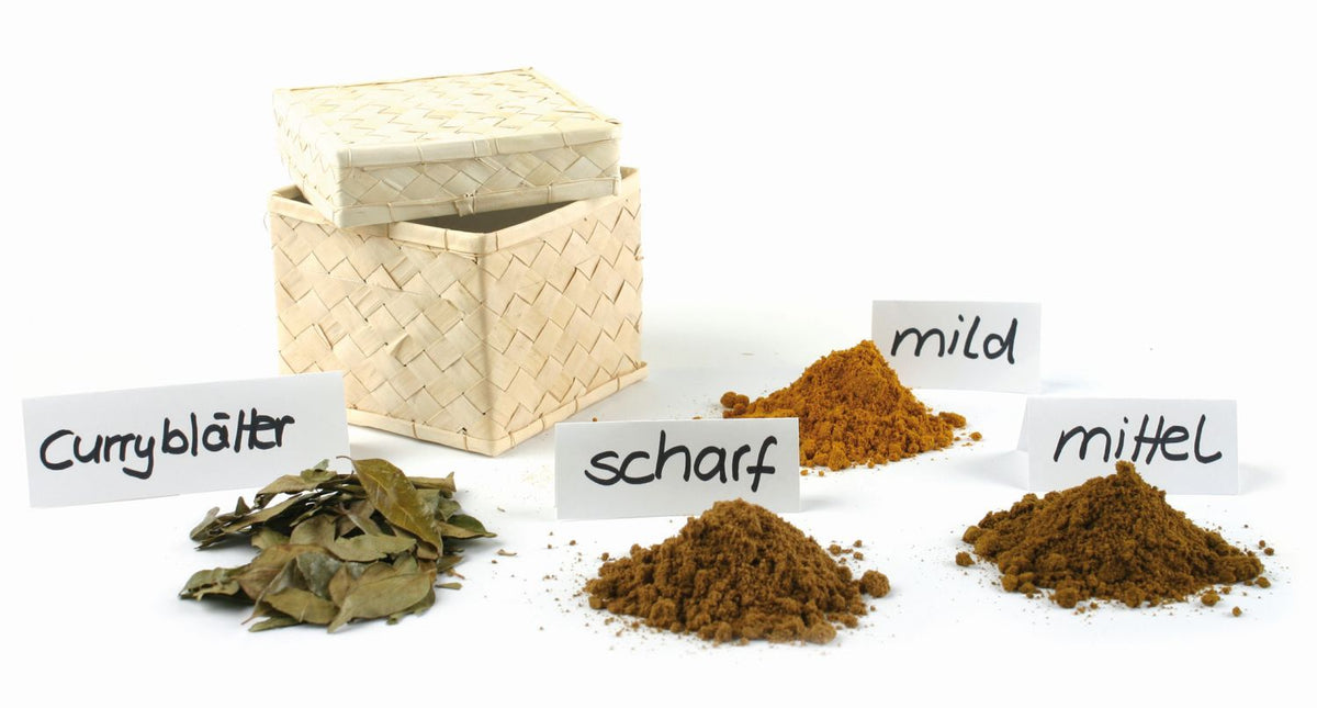 eine geflochtene Palmblattbox mit Deckel, davor Curryblätter und drei verschiedene Curry in unterschiedlichen Schärfegraden