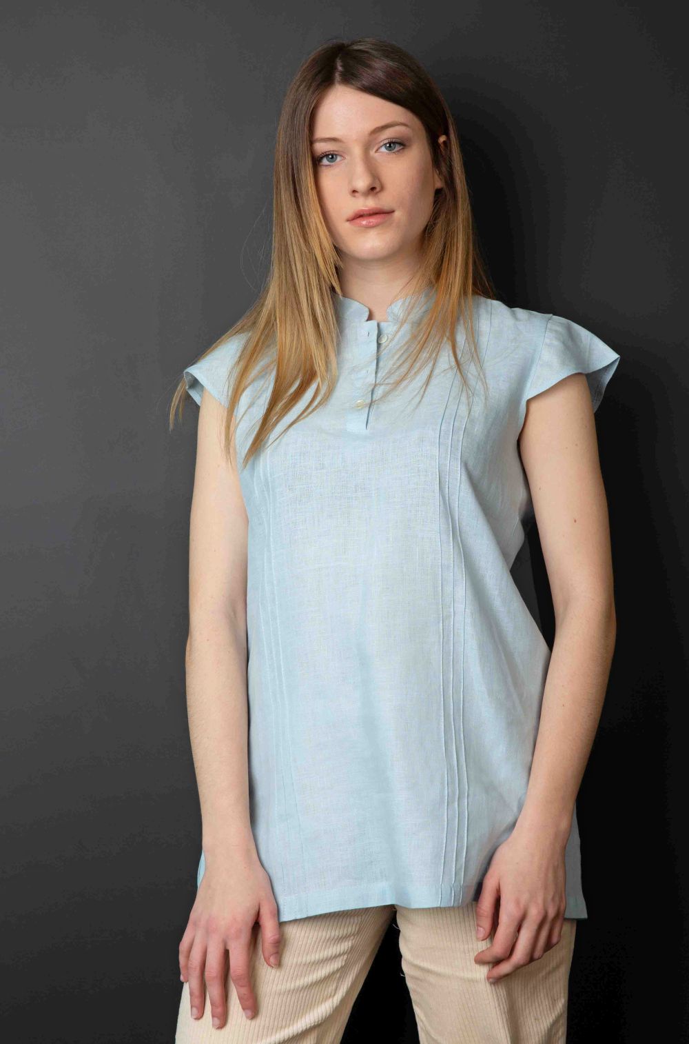 Junge Frau trägt kurzärmelige hellblaue Leinenbluse und beige Cordhose