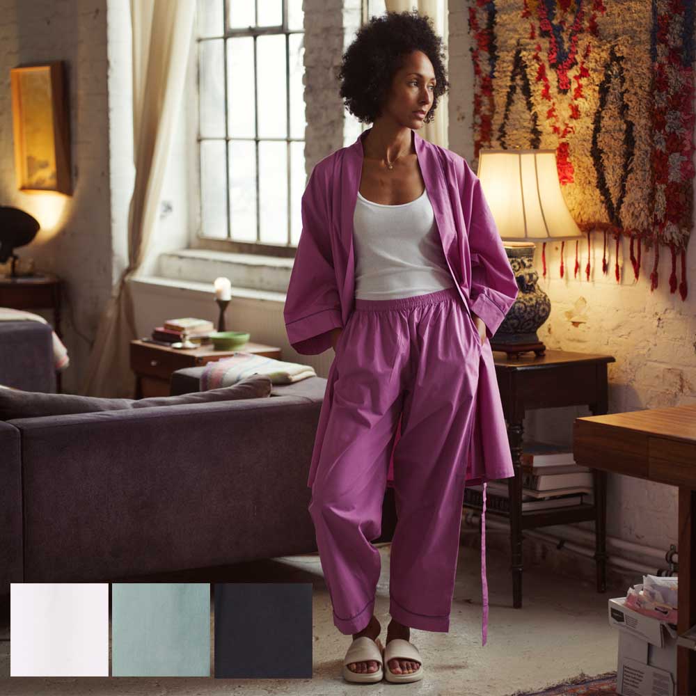 young woman standing in the living room, wearing an open pink kimono with matching pyjama trousers and white T-shirt