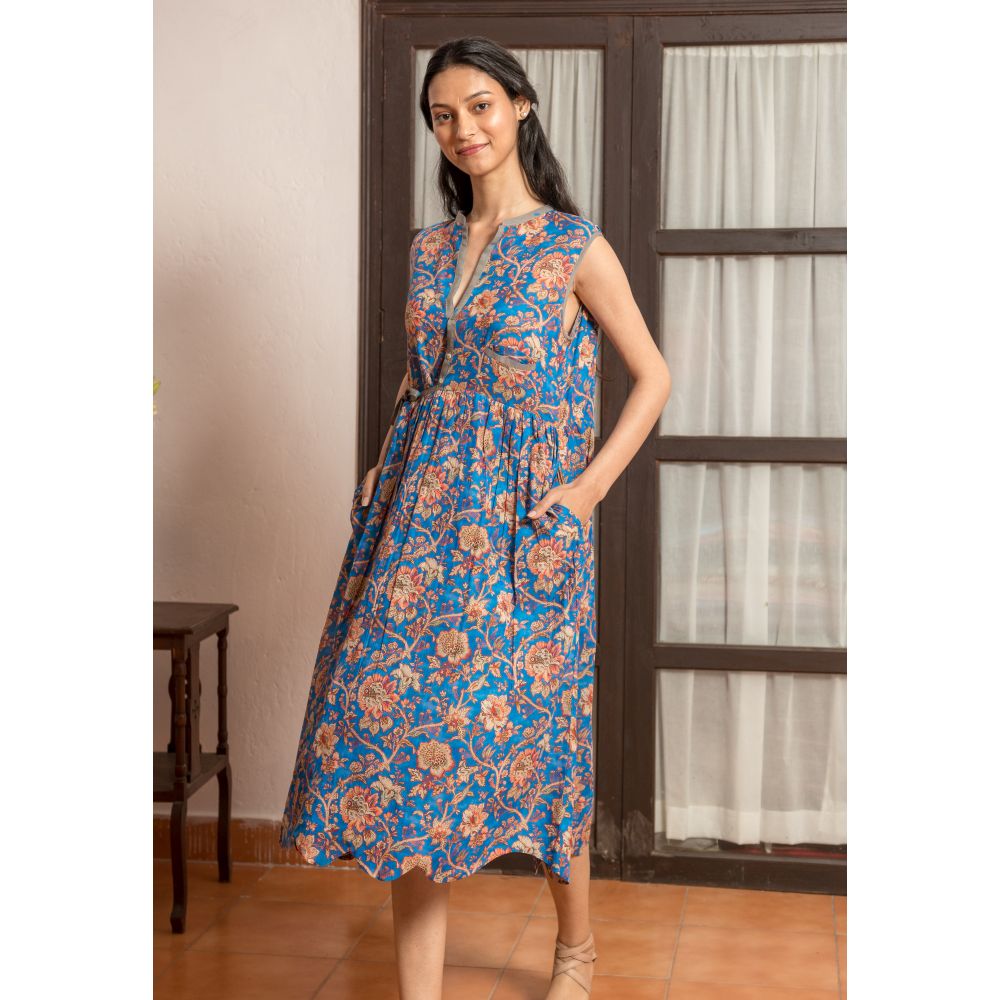 junge Frau trägt ein blaues  ärmelloses Wickelkleid mit braunem Blumenprint und Seitentaschen