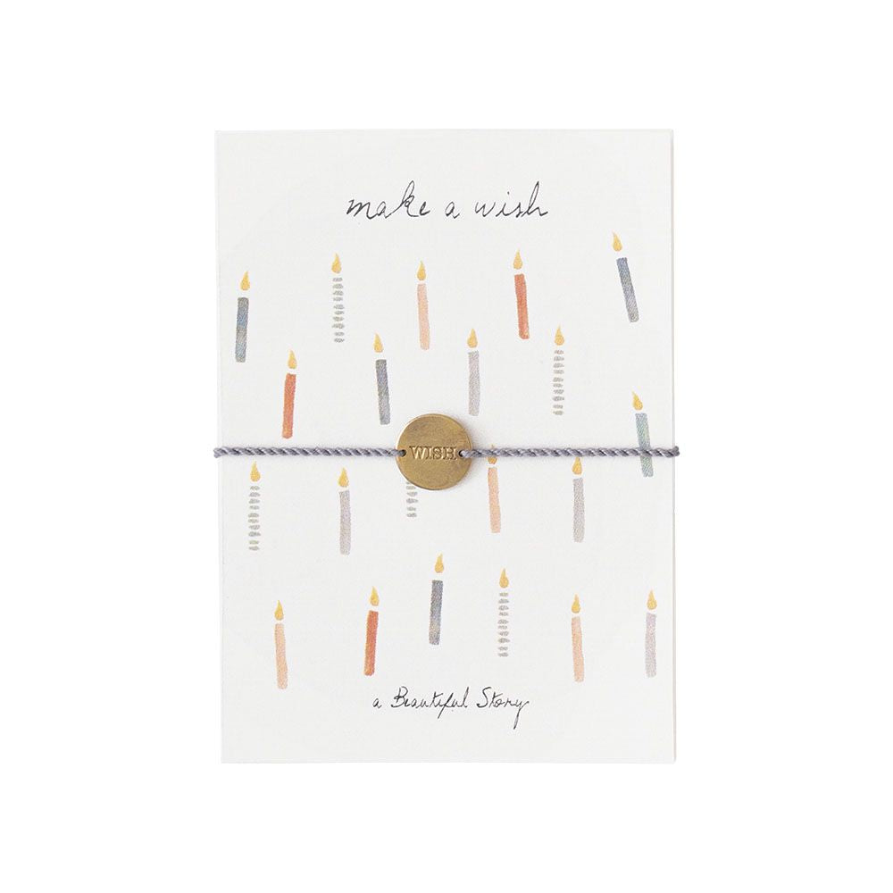 weiße Karte mit verschiedenfarbigen Geburtstagskerzen und mit einem Baumwollarmband umwickellt. Das Armband hat einen Münzanhänger mit der Auftschrift "Wish" 
Oben auf der Karte steh der Text: "make a wish"