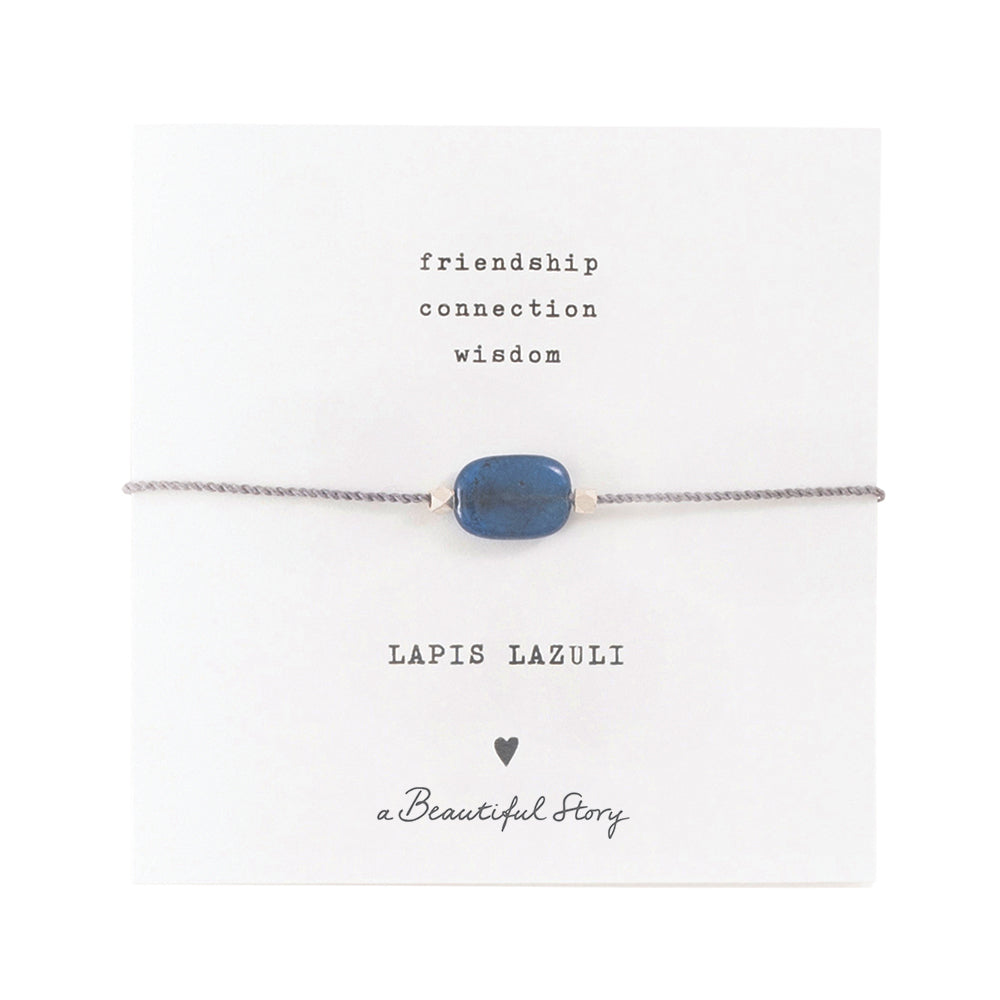 Zartes Armband aus einer silberfarbenden Kordel, mittig ist der blaue Lapislazulistein auf einer kleinen Grußkarte. Oben steht "friendship, connection, wisdom" darunter der Name: Lapis Lazuli, ein Herzchen und "A beautiful Story"