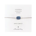 Zartes Armband aus einer silberfarbenden Kordel, mittig ist der blaue Lapislazulistein auf einer kleinen Grußkarte. Oben steht "friendship, connection, wisdom" darunter der Name: Lapis Lazuli, ein Herzchen und "A beautiful Story"