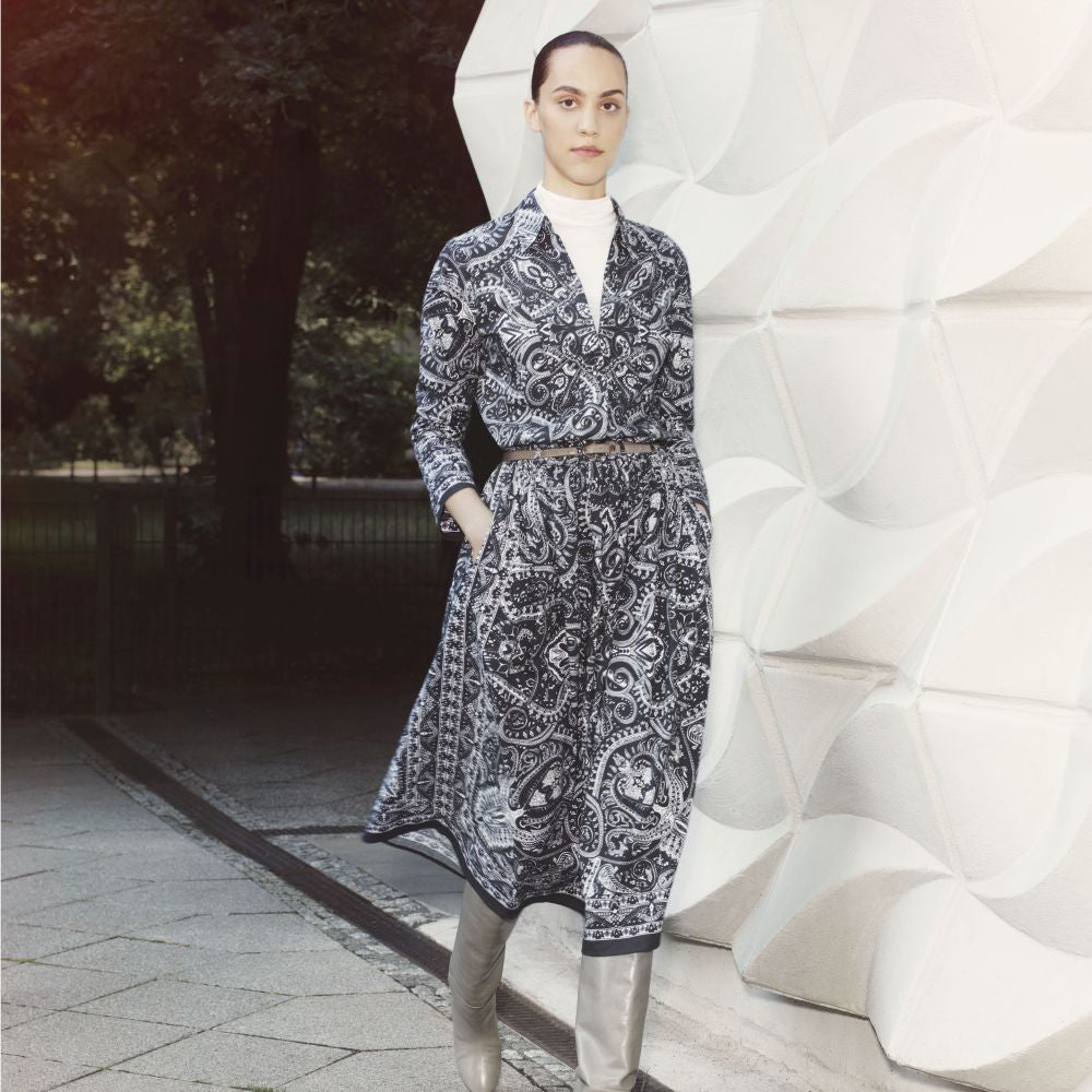 Young woman wearing a black skirt with a white print and a matching blouse. She also wears a brown leather belt, grey boots and a white shirt under the blouse.