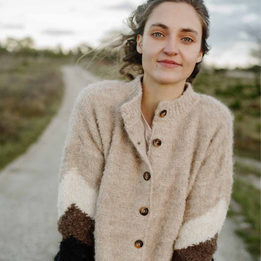 Woman wearing a light brown button-up cardigan with a black and brown and white pattern on the sleeves