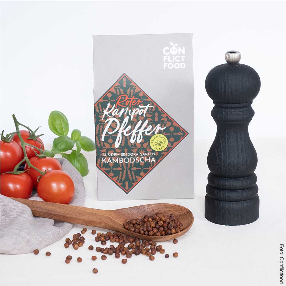 links liegen Strauchtomaten , daneben ein Hollzlöffel mit  Pfeffernkörnern Im Hintergrundsteht eine graue Tüte mir mittigem Etkett, daneben eine schwarze Pfeffermühle
