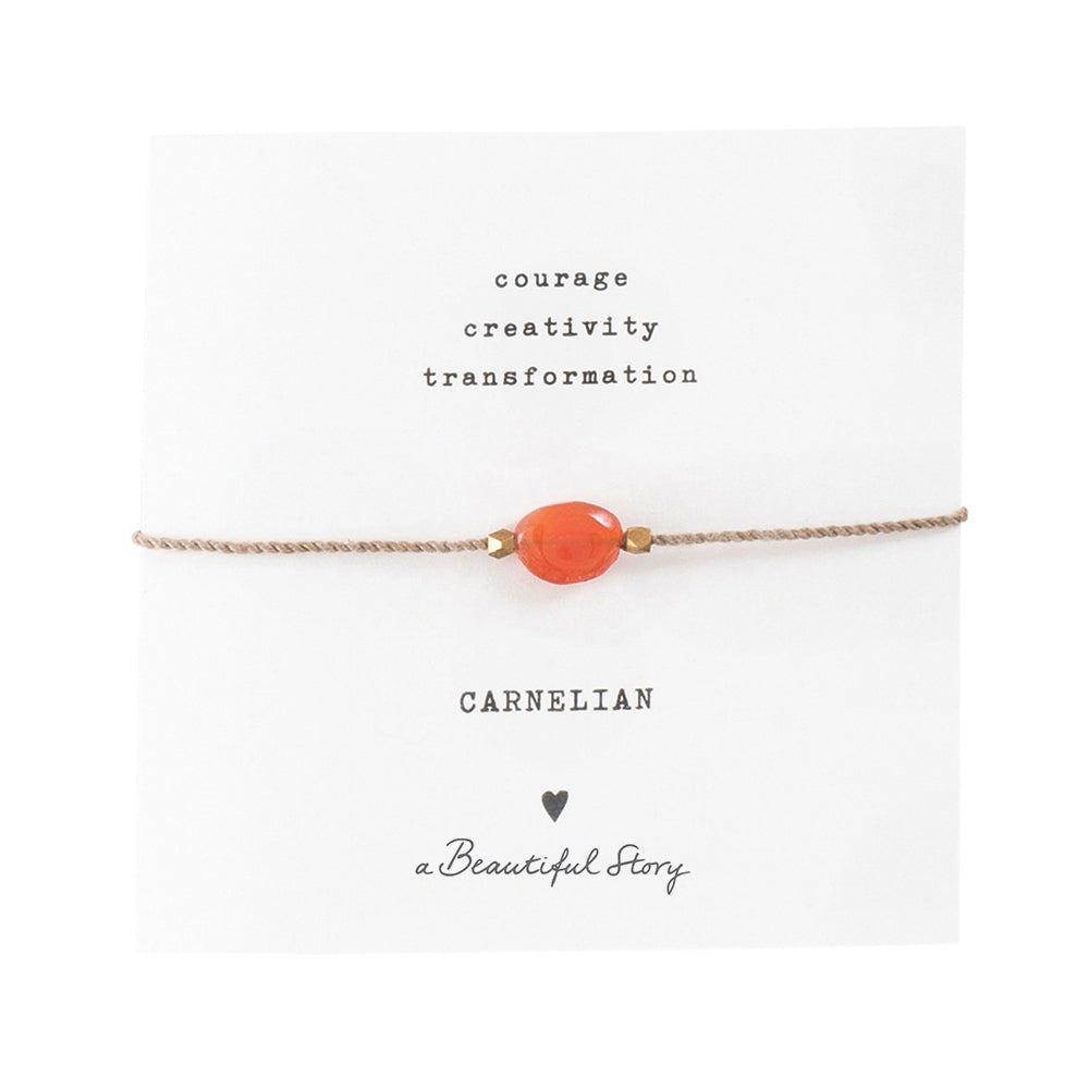 Zartes Armband aus goldfarbender Kordel mit Karneol Edelstein auf Grußkarte. Oben stehen die zugesprochenen Eingenschaften " Courage, Creativity, Transformation" Darunter steht "Carnelian", ein Herzchen und "A beautiful Story"