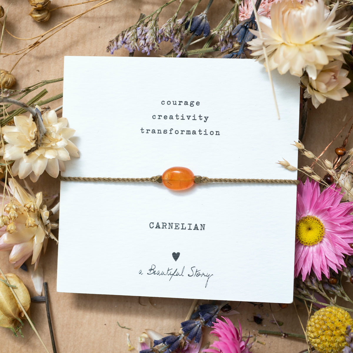 Grußkarte mit Karneolarmband auf einem stimmungsvollem Untergrund: auf Packpapier liegen verstreute Trockenblumen.