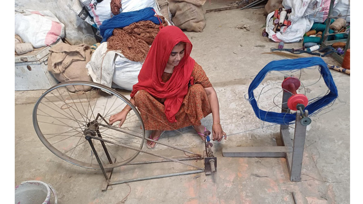 Woman squatting in front of a spool of blue jute yarn.