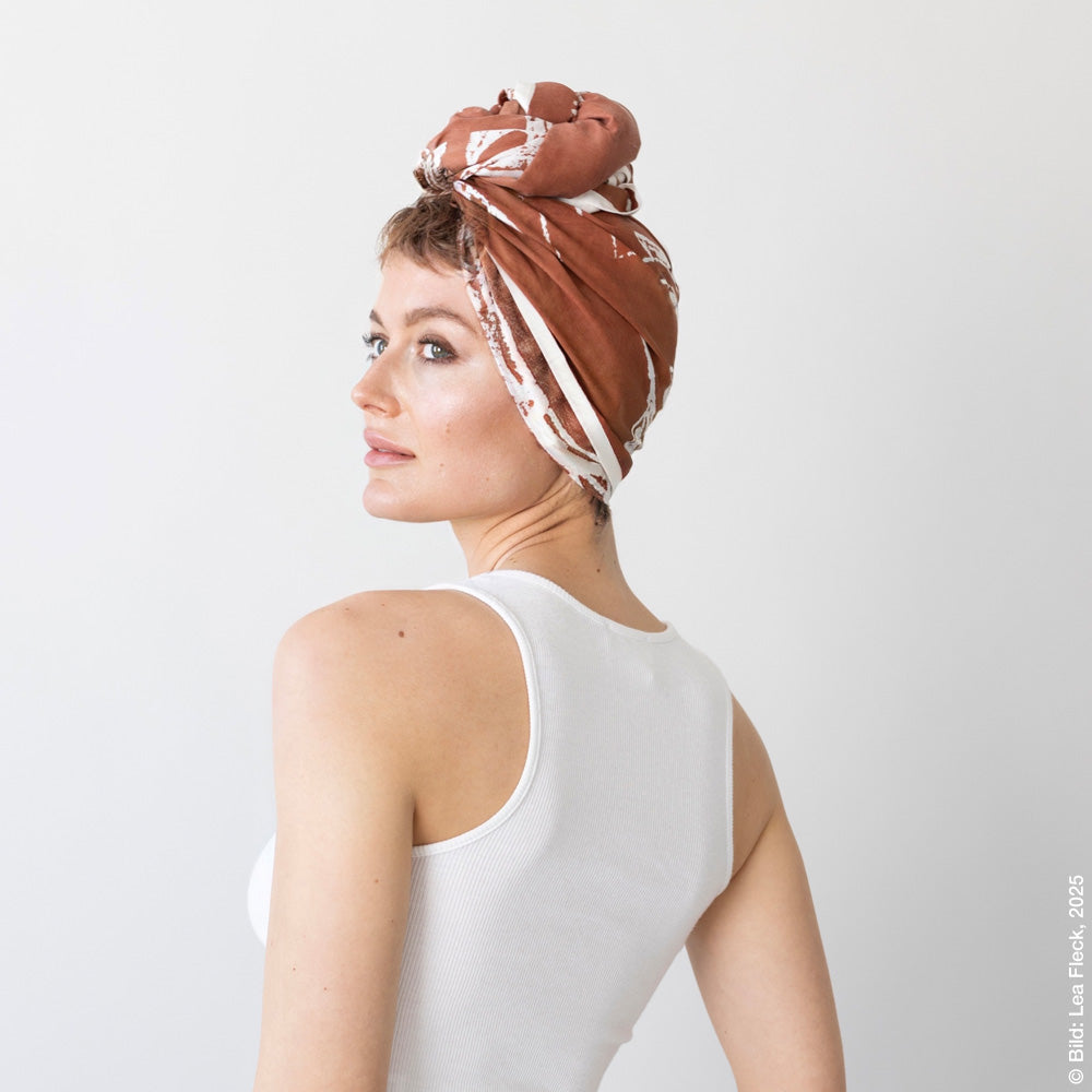 Woman in slightly lateral rear view with a scarf knotted into a turban on her head.