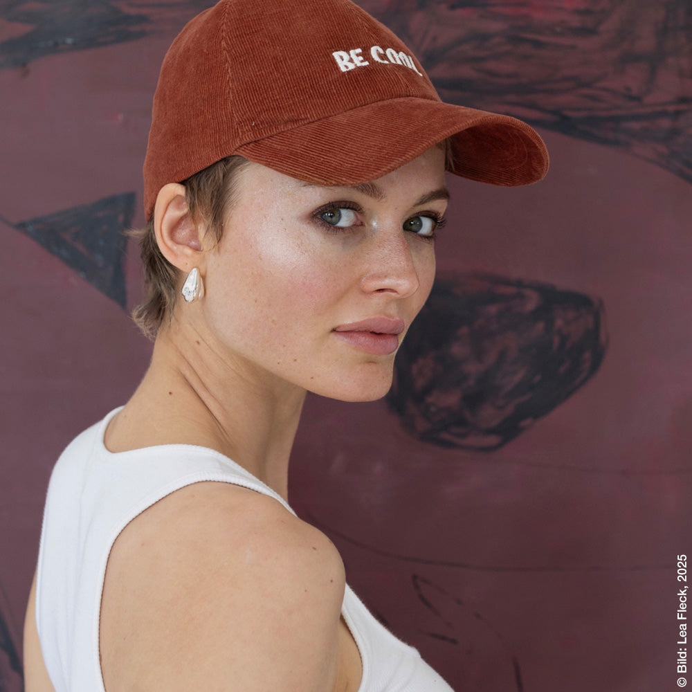 Mühi wearing the cap looking over her shoulder in front of one of her pictures.