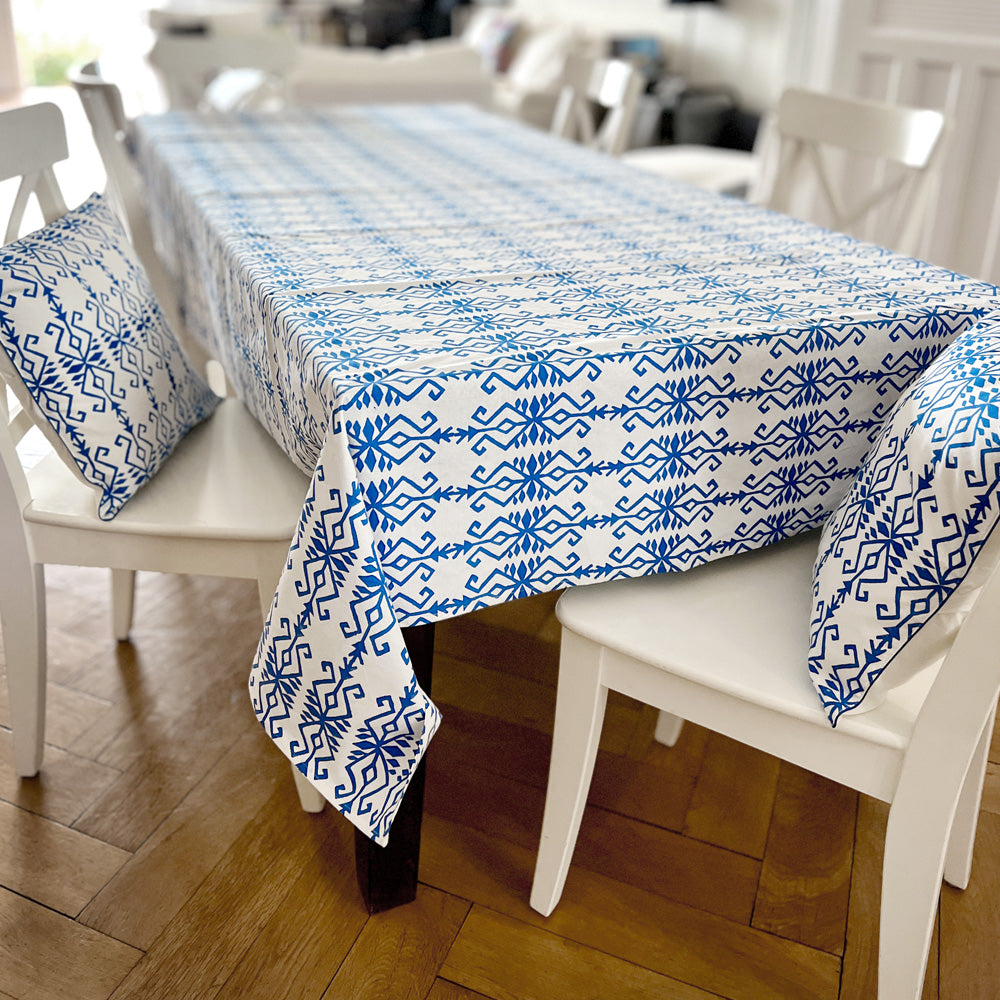 Large dining table with white and blue patterned tablecloth. Two chairs with matching cushions.