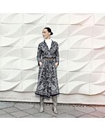 junge Frau in trägt einen schwarzen Rock mit weißem Print und einer gleichen Bluse. Dazu trägt sie einen braunen Ledergürtel, graue Stiefel, unter der Bluse ein weißes Shirt.