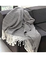schwarz-weiß gemustertes Alpaka Plaid mit weißen Fransen auf einem grauen Sofa