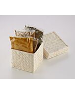 Opened woven palm leaf box with three bags of different curries and a bag of curry leaves, with the lid behind it