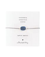 Zartes Armband aus einer silberfarbenden Kordel, mittig ist der blaue Lapislazulistein auf einer kleinen Grußkarte. Oben steht "friendship, connection, wisdom" darunter der Name: Lapis Lazuli, ein Herzchen und "A beautiful Story"