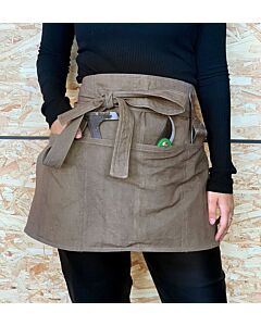 Bildausschnitt einer Person im schwarzen Pullover, die eine braune Schürze mit mehreren Taschen trägt, in denen Gartenutensilien stecken, die rechte Hand befindet sich ebenfalls in einer Schürzentasche, die Schürze ist mit einer Schleife zugebunden