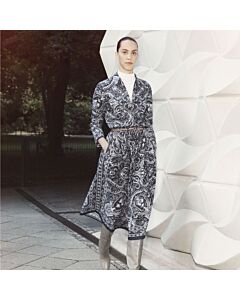 Junge Dame mit schwarz weiß gemusteter Bluse und gleichem Rock, sie trägt einen schmalen Gürtel und graue, knielange Stiefel dazu