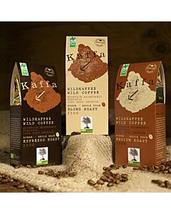 drei  verschiedenfarbige Kafeetüten mit Wildkaffe unterschiedlicher Varianten. Vor den Tüten liegen Kafeebohnen