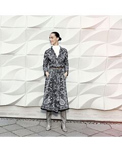 junge Frau in trägt einen schwarzen Rock mit weißem Print und einer gleichen Bluse. Dazu trägt sie einen braunen Ledergürtel, graue Stiefel, unter der Bluse ein weißes Shirt. 