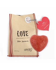 braune Papiertüte, links drei rote Streifen, mittig in Schwarz die Aufschrift "LOVE", oben rechts befindet sich ein roter Papieraufhänger in Herzform, darunter ein Stück rote Seife in Herzform