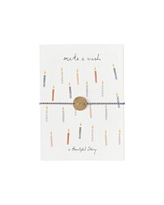 weiße Karte mit verschiedenfarbigen Geburtstagskerzen und mit einem Baumwollarmband umwickellt. Das Armband hat einen Münzanhänger mit der Auftschrift "Wish" 
Oben auf der Karte steh der Text: "make a wish"