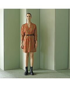junge Frau in einem kurzen braunen Kleid mit orangefarbenem Muster, sie trägt einen braunen Gürtel um die Tailie sowie schwarze Kurzstiefel