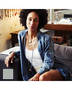 Frau auf dem Sofa mit einem aufgenköpften blauen Kleid mit Stickerei am Ärmel, darunter trägt sie ein weißes Top