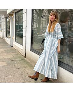 junge Frau in einem hellblau-weß gestreiften Oversized Sommerkleid steht angelehnt an einem Schaufenster